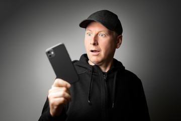 Man in black shocked with the message on the phone or phone itself