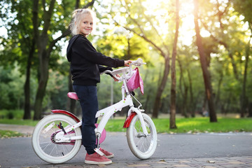 Cute adorable beautiful caucasian little blond girl enjoy riding white small bicycle by path in green summer city park forest or garden at bright sunny day outdoor. Children healthy lifestyle concept