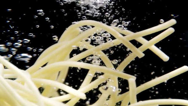 Pasta vortex, spaghetti spinning in the boiling water with bubbles on black background. Slow motion