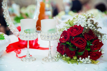 There are drops of water on the roses . Wedding rings are placed on the red roses . The rings are in the middle of the cups . Wedding bouquet of red flowers.