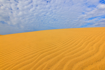 Summer dry landscape in Africa. Black pebble stones. Sandy waves in the wild nature. Dunas Maspalomas, Gran Canaria, Spain. Beautiful rare blue sky with white clouds.