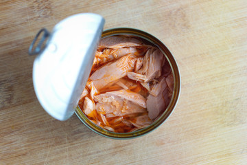 Close up of open canned tuna in red oil on wooden table, top view
