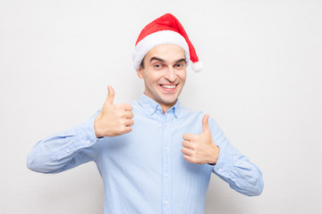 Fototapeta na wymiar Concept of a new year. Cheerful man in Santa hat shows thumbs up, portrait, white background