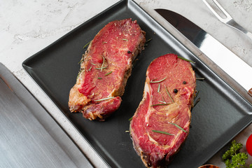 Marinated raw steaks on stone table with spices