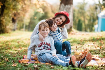Fototapeta premium Such love, which is impossible to describe, only to feel. Mothers and sons. Happy Mother's Day! Mother hugs her children on a background of forest. Family. Mom and children are sitting on the mat.