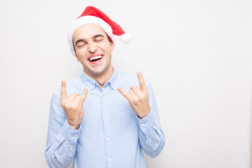 Joyful man in Santa Claus hat showing goat gesture, portrait, white background, copy space