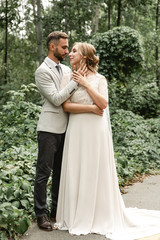 portrait of a happy wedding couple on their wedding day,beautifully dressed newlyweds tenderly hug while walking in a park,handsome bearded groom gently hugs his bride