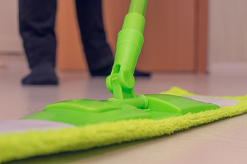 Mop in the foreground, guyl washes the floor in his house, men's legs, close up, toned, cropped image
