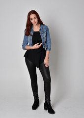  portrait of a pretty girl with red hair wearing black leather pants and top. Full length standing pose isolated against a  grey studio background