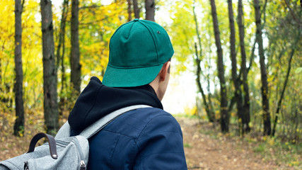Man with backpack walking uphill through the forest, rear view, close up, 16:9