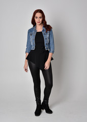  portrait of a pretty girl with red hair wearing black leather pants and top. Full length standing pose isolated against a  grey studio background