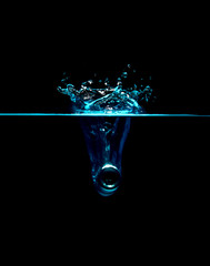 The object falls into the water, causing scattered waves, causing many blue bubbles in the water to reach a dark background.