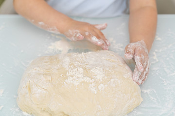 hands of a young child on a yeast dough in flour. the child learns to cook