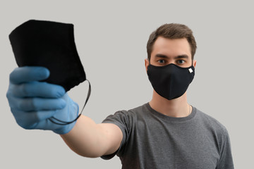Young european man wearing reusable mask against the corona virus covid 19  man wearing surgical mask to prevent from virus white\grey background Corona virus pandemic