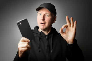 Man in black clothes happily surprised with the message on the phone or phone itself