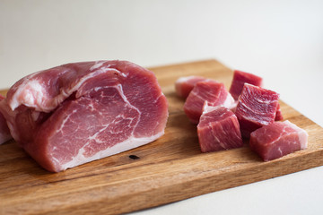 Fresh pork meat, pieces of different sizes on a wooden stand on a light background