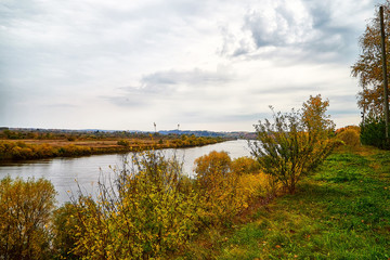 View on the river from top place on the bank through branch of trees and sky with clouds background. Nature landscape in an autumn day