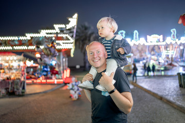 Father and his piggybacked little son enjoying funfair.