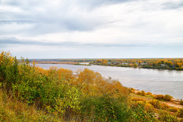 View on the river from top place on the bank through branch of trees and sky with clouds background. Nature landscape in an autumn day