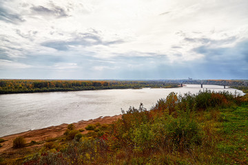 View on the river from top place on the bank through branch of trees and sky with clouds background. Nature landscape in an autumn day