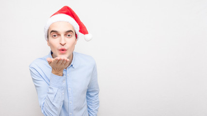 Attractive man in Santa Claus hat blows air kiss, portrait, white background, 16:9