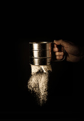 Mesh flour sifter working in cook’s hand - black background