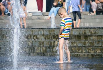 Little boy playing with fountain water jets at the square