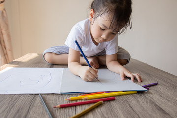 Naklejka premium Photos from above and selective focus of beautiful and adorable preschooler is drawing rainbow on white paper placed on a wooden table by color pencils for learning to develop creativity and emotion.