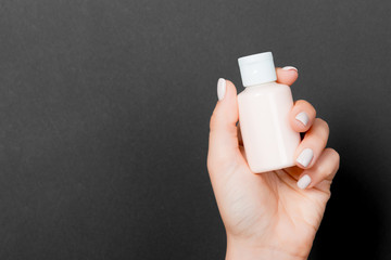 Woman's hand is holding a cosmetics bottle at black background with copy space for your design