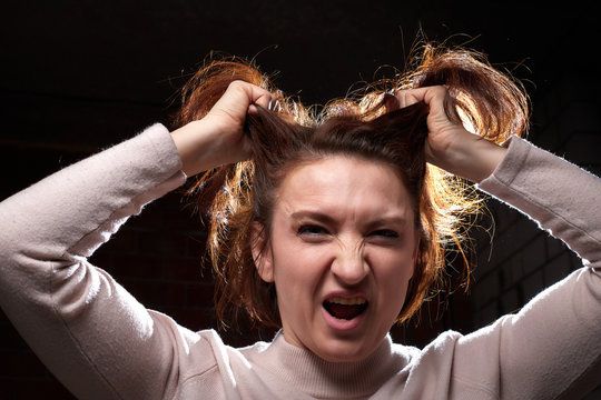 Emotional portrait of middle age woman on black background. Female model geting angry toughting her hair while posing in the Studio