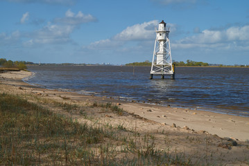 scenic white lighthouse on the island Elsflether Sand in the river Weser seen behind the beach during high tide  in front of vivid blue sky with white clouds