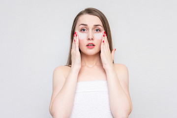 Upset woman using white under eye patches, white background. Concept of eye skin treatment