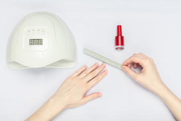 White uv-lamp and woman's hands during manicure, white background, copy space, top view. Manicure and nail Polish concept