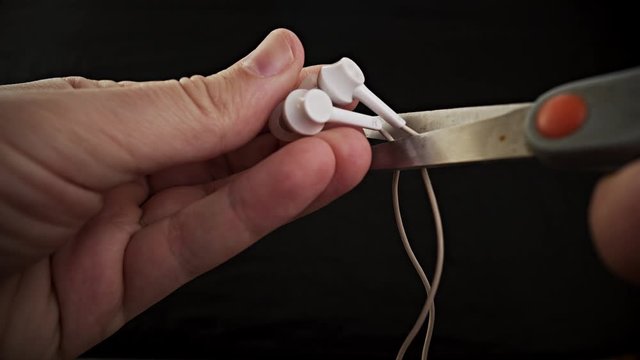 Hands holding the scissors to cut the headphone