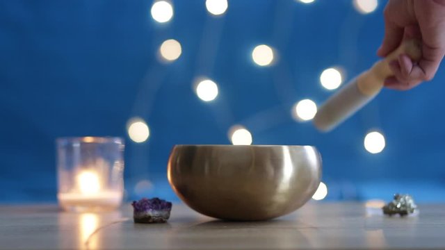 A Tibetan singing bowl is used for spiritual practices. Woman playing Tibetan singing bowl at the table with candle and crystals. Meditative concept. Meditation at home, alternative medicine. 