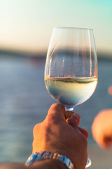 Man holding a glass of white vine next to a lake