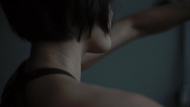 Fit dancer turns away from camera on the floor warming up and stretching in dark moody dance studio, medium close