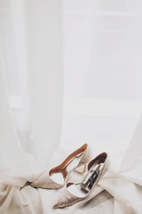 Modern wedding shoes on tulle in soft morning light. Stylish luxury beige shoes with lace floral pattern on window. Bridal morning preparations and boudoir