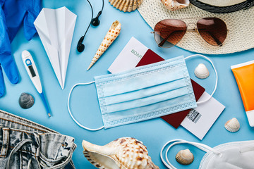 Overhead view of coronavirus travel accessories on blue background. Essential summer vacation items...