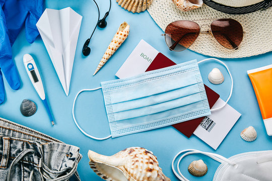 Overhead view of coronavirus travel accessories on blue background. Essential summer vacation items during the coronavirus pandemic. Covid-19 and travel concept.