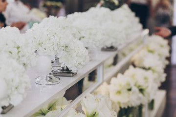 Modern decor at wedding reception in restaurant. Stylish white hydrangea and modern white candles with light at tables. Luxury catering