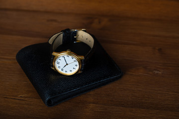 Retro golden wristwatch with Roman numerals on the dial lie on a black leather wallet.