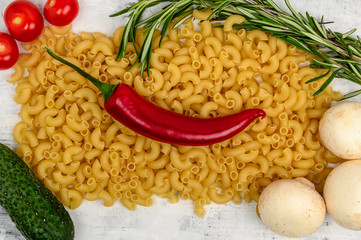 Macaroni, chili peppers and mushrooms and tomatoes are on the table.