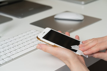 Close up of woman's hands in gloves wiping smartphone screen with disinfectant cloth