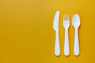 Plastic white cutlery set with yellow background. Top view