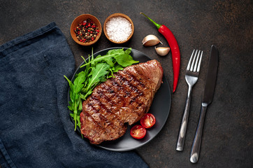 delicious grilled beef steak with spices and herbs on a black plate on a stone background