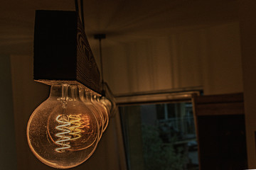 Stare old school lampy z żarnikiem w kształcie spirali ustawione w rzędzie na drewnianej belce świecące ciepłą barwą oświetlają pokój