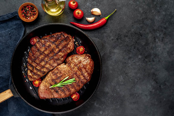 Two grilled beef steaks in a pan with spices on a stone background