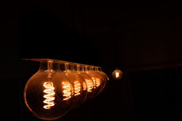 Stare old school lampy z żarnikiem w kształcie spirali ustawione w rzędzie na drewnianej belce świecące ciepłą barwą oświetlają pokój - obrazy, fototapety, plakaty