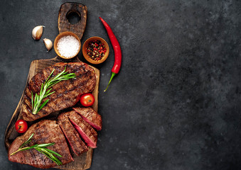 Two grilled beef steaks with spices and herbs on a cutting board on a stone background with copy space for your text